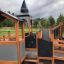 Dřevěné Campanille playground castle se skluzavkami a lezeckými konstrukcemi v parku.