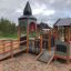 Campanille playground castle se skluzavkami a lezeckými prvky v parku.