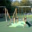 Double Safety Seat double swing na hřišti s lezeckou konstrukcí v pozadí.