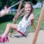 Double Safety Seat double swing s dětmi hrajícími si v pozadí