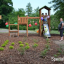 Triangle Modern Nature wooden playhouse with slide v prostředí parku s hrajícími si dětmi.
