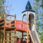 Alcazar playground castle se skluzavkou a lezeckou konstrukcí v parku.