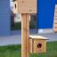 Bird feeder se dvěma dřevěnými budkami pro ptáky upevněnými na svislém sloupu.