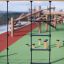 Ural climbing net na venkovním hřišti s dřevěnými konstrukcemi v pozadí.
