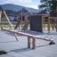 Dřevěné Nature Seesaw na moderním hřišti s lezeckými konstrukcemi v pozadí.