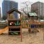 Jungle House playhouse with slide na hřišti s městskými budovami v pozadí.
