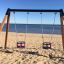Double Baby Swing umístěné na písečné pláži s výhledem na moře.