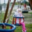 Double Baby Swing s miminkem v růžovém oblečku, které si užívá jízdu na hřišti.