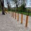 Agility Weave Poles instalované venku na štěrkovém povrchu se stromy v pozadí.