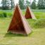 Přístřešek na dětské hřiště Tipi Nature wooden house z přírodního dřeva na travnatém poli.