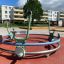 Bicycle merry-go-round na dětském hřišti s bytovými domy v pozadí.