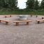 Robinia bench umístěné kolem centrálního ohniště ve venkovním parkovém prostoru.