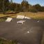 Skatepark s curb sloping výškou 15–25 cm, rampami a railami na asfaltovém povrchu v travnaté oblasti.