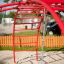Červený Cross Climber steel structure na hřišti s pískem a visícím lanem.