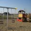 Baby Double Swing na hřišti s herním domkem a lezeckou konstrukcí.