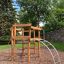 Sherwood wooden playhouse v parku se stromy a kamennou zdí v pozadí.
