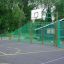 Venkovní basketbalové hřiště se zelenými kovovými ploty, s basketbalovým vybavením Shea.