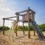 Kampinos wooden playhouse se skluzavkami a lezeckou sítí na pískovém hřišti.
