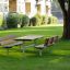 Table & Bench v zeleném parkovém prostředí se stromy a budovami v pozadí