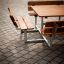 Venkovní sada Table & Bench Quadro s dřevěnými sedáky a kovovým rámem na dlážděném povrchu.