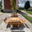 Venkovní dřevěná sada Table & Bench Quadro na dlážděné ploše se zelení v pozadí