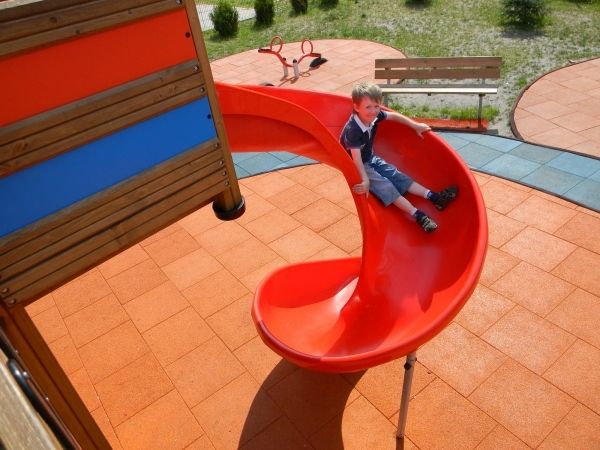 Dítě si hraje na červené spirálové skluzavce na Rubber Tiles 90