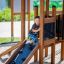 Dítě si hraje na Knight's Castle Nature playhouse with slide.