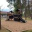 Knight's Castle Nature playhouse with slide v zalesněné části hřiště.