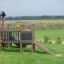 Fortress Nature playhouse with slide na travnatém poli s hrajícími si dětmi