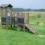 Fortress Nature playhouse with slide na zeleném poli s hrajícím si dítětem.