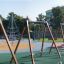 Swing Frame (double swing) na barevném hřišti s dalšími herními prvky v pozadí