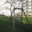 Swing Frame (single swing) na dětském hřišti s obytnými budovami v pozadí.