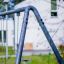 Swing Metal Frame (single swing, wide) ve venkovním prostředí s rozmazanou bílou budovou v pozadí.