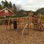 Panther wooden playhouse na pískovém hřišti s lezeckými konstrukcemi a skluzavkami.