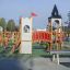 Tintagel playground castle se skluzavkami a lezeckými konstrukcemi za slunečného dne.