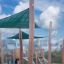 Sun Shade Triangle 3x3x3 Nature (Robinia) instalované v prostoru hřiště s dřevěnými podpěrami.