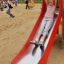 Dítě sjíždí po Single Swing with Tower single slide na hřišti.