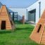 Wigwam wooden house na zelené trávě poblíž moderních budov