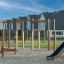 Dřevěná lezecká konstrukce Horizontal Ladder Large na hřišti s pískovým povrchem a obytnými domy