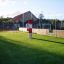 Ball catcher na zeleném hřišti s oplocením a budovou v pozadí.