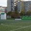 Shelter herní domeček na sportovním hřišti s městskými budovami v pozadí.