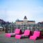 Růžový Lounge chair umístěný na dřevěné terase s panoramatem města v pozadí.