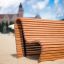 Dřevěná Sofa Wave lavička na písečné pláži s budovou v pozadí.
