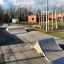 Skatepark s rampami vedle dětského hřiště a budovami v pozadí.