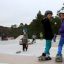 Děti si užívají skateboarding ve venkovním skateparku s rampami.