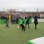 Děti hrající fotbal na sportovním hřišti Multiarena, sledované davem.