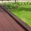 Rubber Tiles 55 bezpečnostní podlaha hřiště v tmavě červené barvě vedle zelené trávy a rostlin