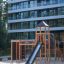 Dřevěná herní konstrukce Explorer castle with slide na pískové ploše před moderní budovou