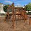 Kiosk Modern Nature wooden playhouse na pískovém hřišti obklopeném budovami a stromy.