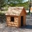 Dřevěný Nature Playhouse na hřišti obklopeném stromy.